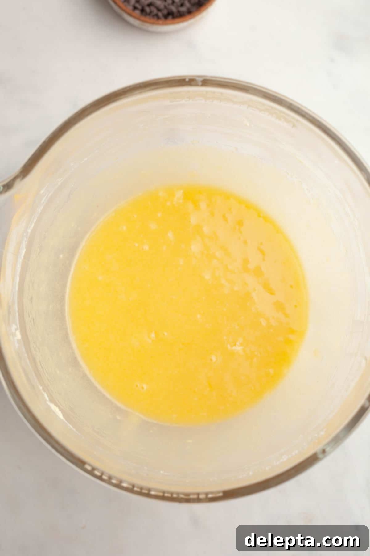 Red Velvet Chocolate Chip Indulgence 6 A large glass mixing bowl holding a light yellow, smoothly blended cake batter after the eggs, oil, vanilla, and vinegar have been incorporated.