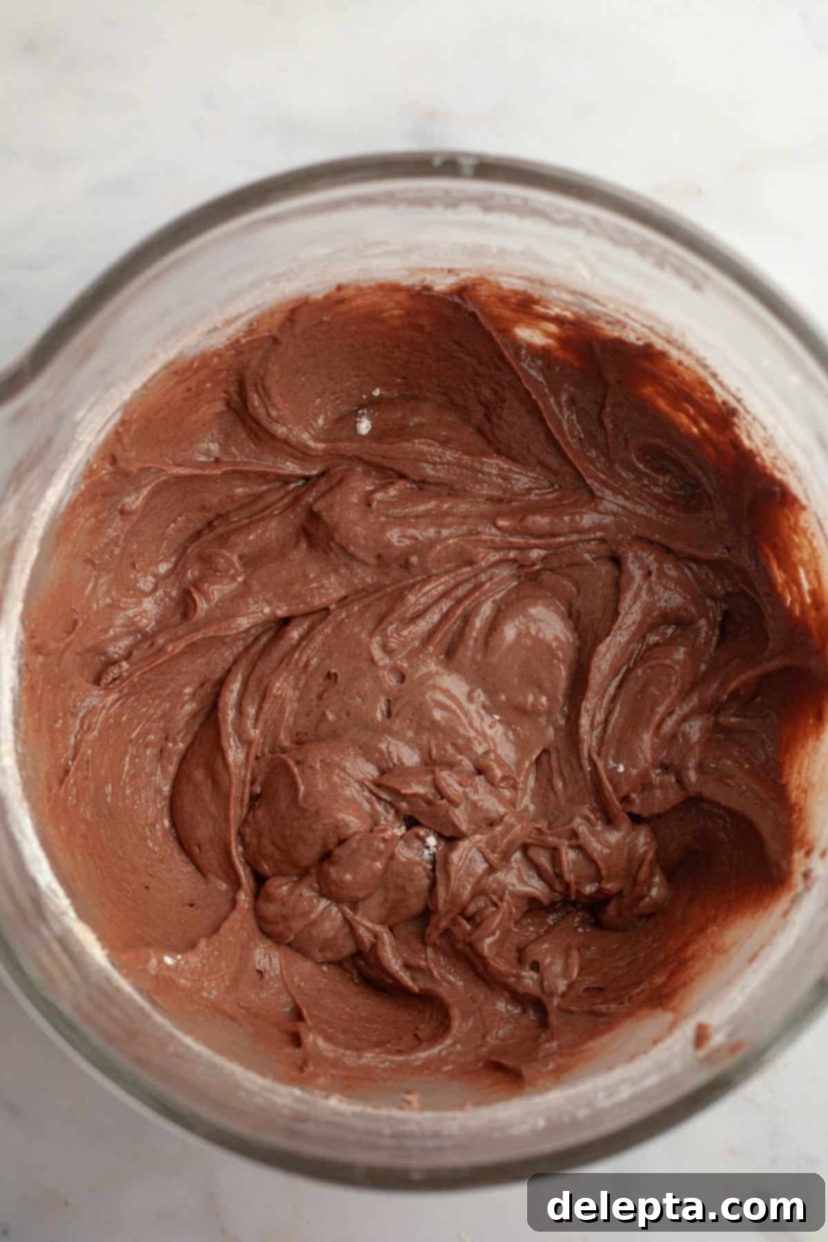 Red Velvet Chocolate Chip Indulgence 7 A large glass bowl containing a slightly brownish, thick cake batter, indicating the flour mixture has been partially incorporated before the red food coloring is added.