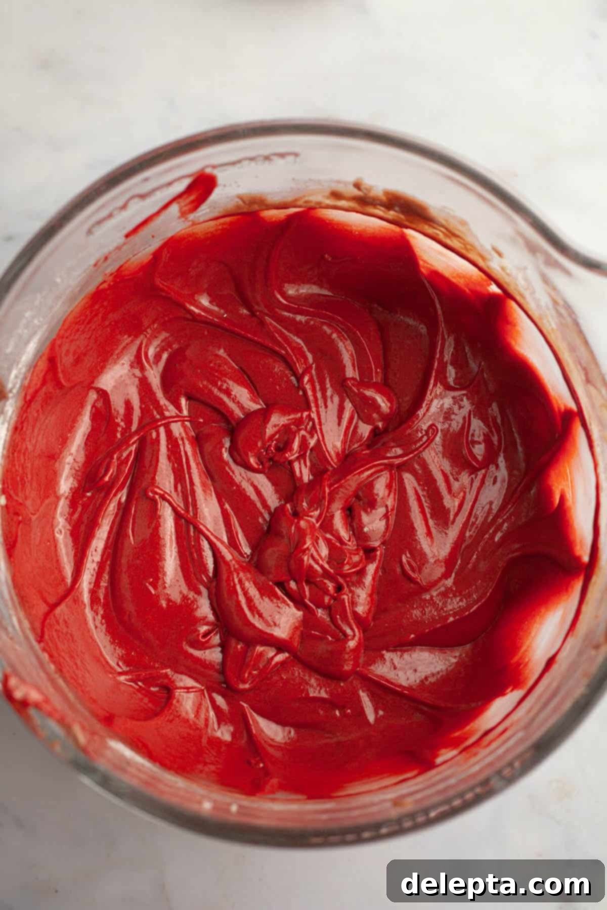 Red Velvet Chocolate Chip Indulgence 8 Vibrant red velvet cake batter swirling in a large glass mixing bowl, having just been mixed with the food coloring.