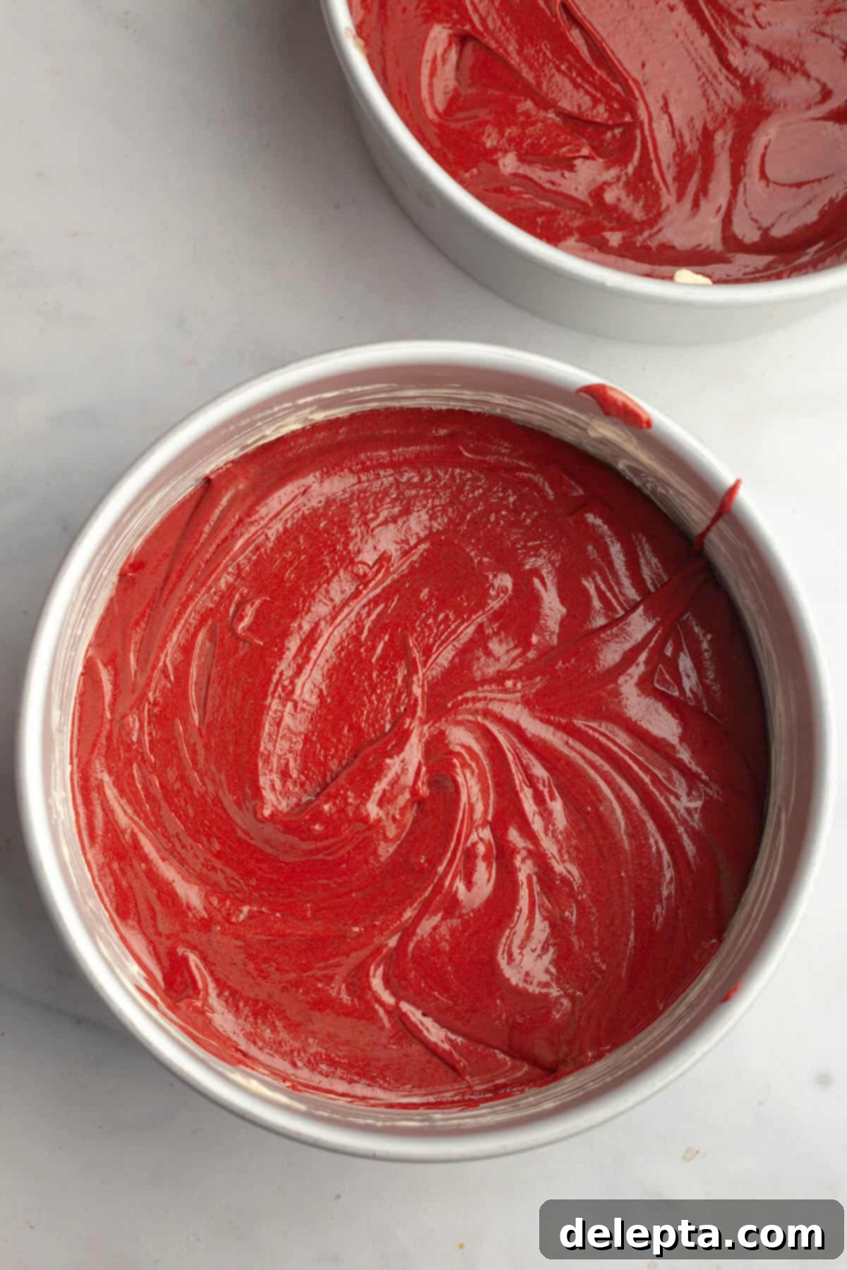 Red Velvet Chocolate Chip Indulgence 9 Two round cake pans, perfectly prepared and filled with evenly distributed vibrant red velvet cake batter, ready for baking.