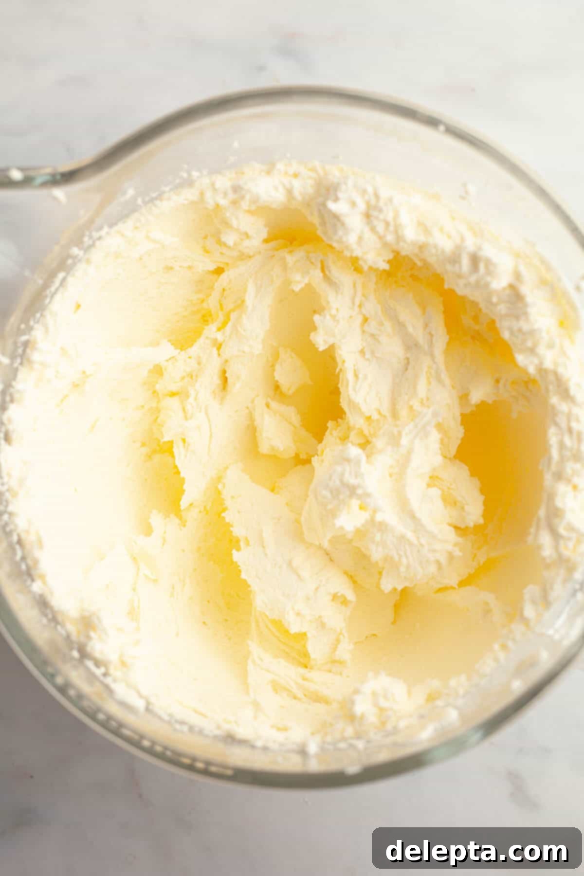 Red Velvet Chocolate Chip Indulgence 10 A large glass mixing bowl containing light yellow, fluffy cream cheese frosting, showing its creamy texture before chocolate chips are added.
