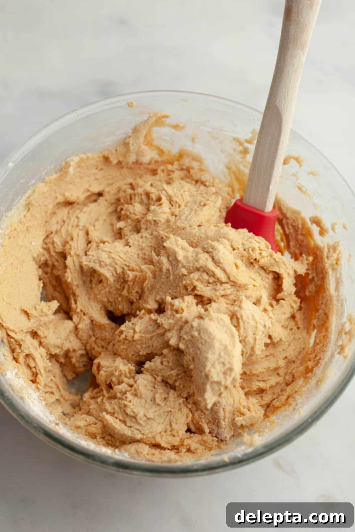 Peanut Butter Snickerdoodle Bliss 7 Peanut butter cookie dough in a bowl being gently mixed with a rubber spatula, showing its soft consistency.