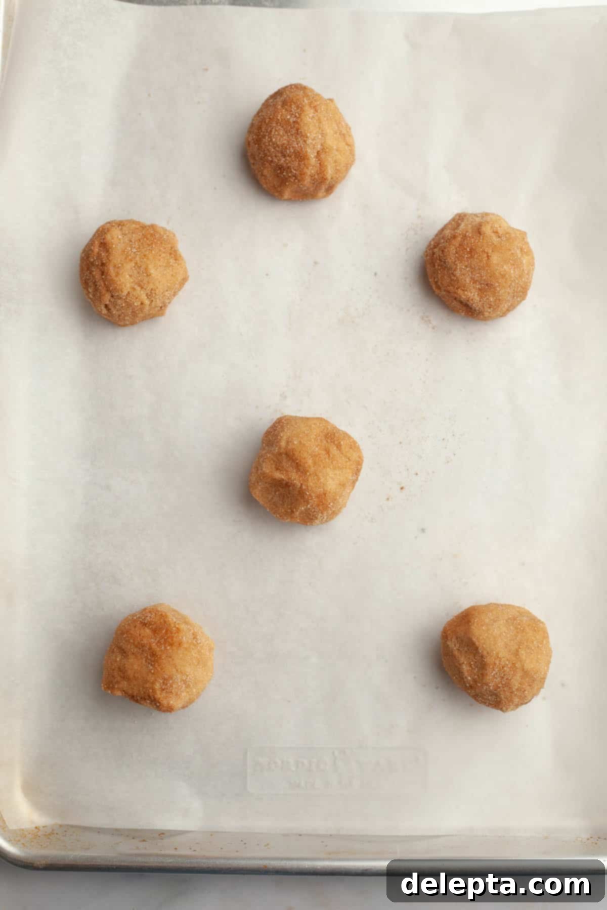 Peanut Butter Snickerdoodle Bliss 8 Raw peanut butter snickerdoodle cookie dough balls, coated in cinnamon sugar, arranged on a parchment-lined baking sheet.