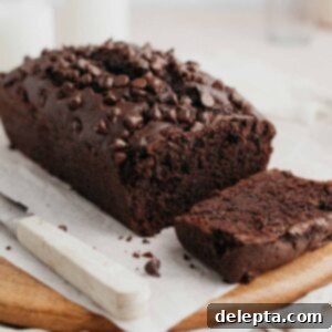Velvety Chocolate Sour Cream Pound Cake 8 A perfect chocolate loaf cake on parchment paper, studded with chocolate chips, with one inviting slice already cut, showcasing its moist texture.
