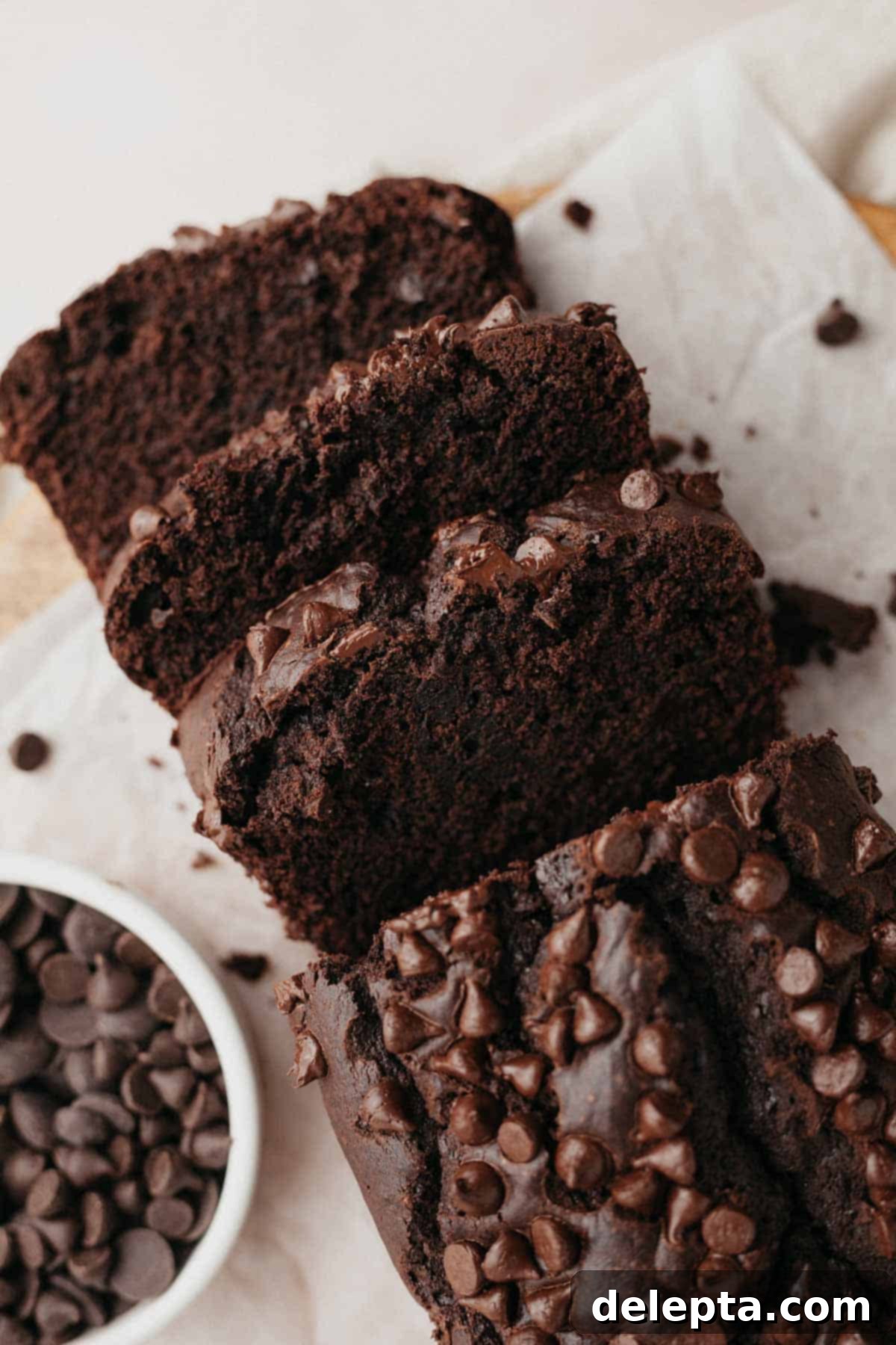 Velvety Chocolate Sour Cream Pound Cake 7 An inviting overhead shot of a freshly baked chocolate loaf cake, generously topped with chocolate chips, with three perfect slices already cut, ready to be served.