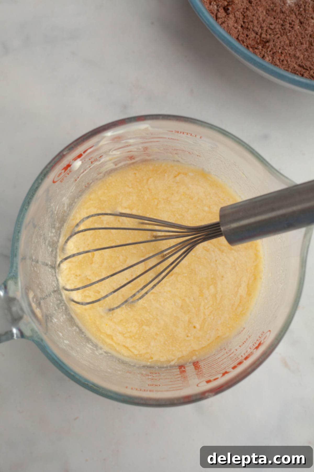 Peppermint Chocolate Dream Cupcakes 5 A large glass jug with a whisk and a yellow batter in it, prepared for mixing.