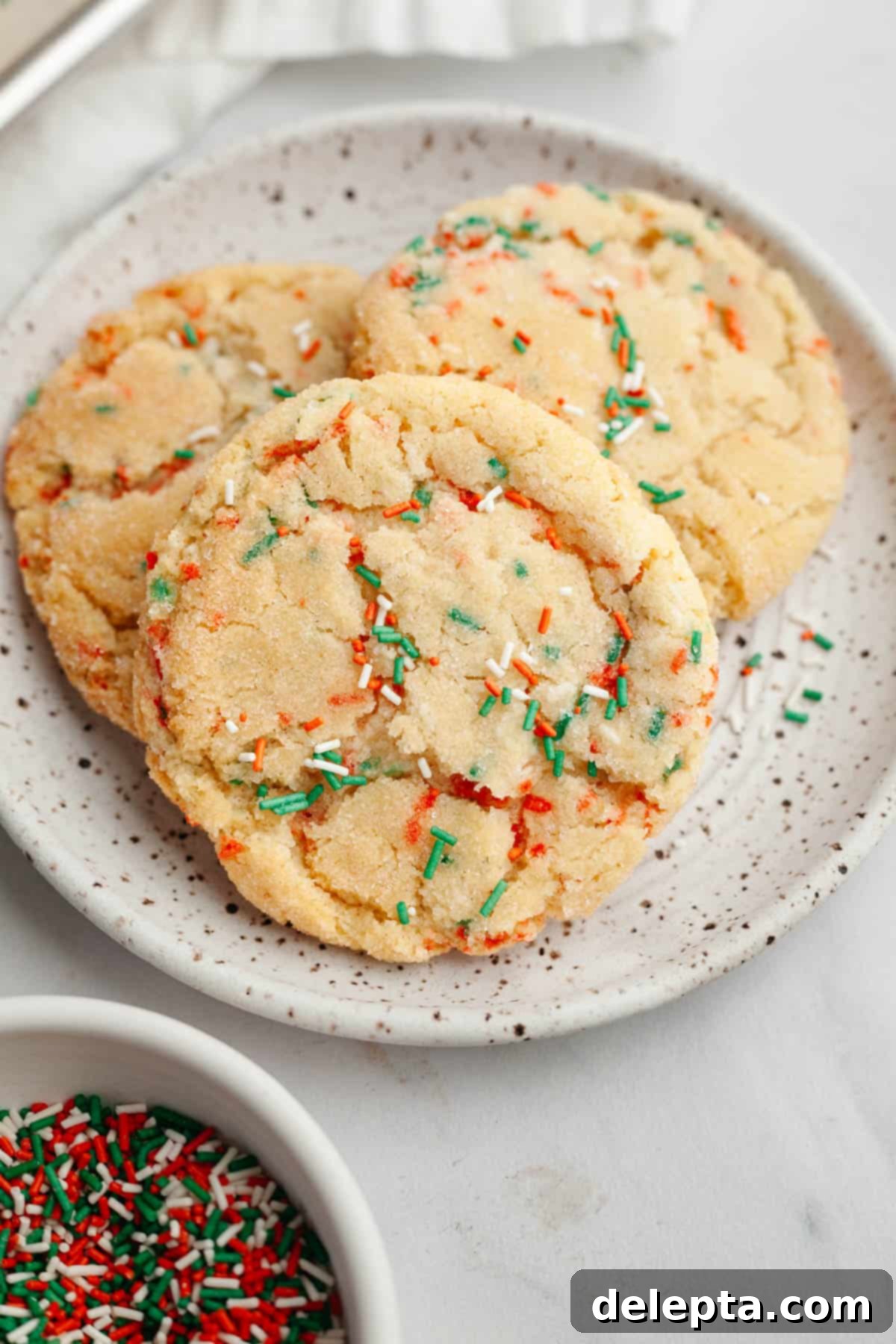 Melt-in-Your-Mouth Brown Butter Christmas Sprinkle Cookies 11 A small plate with three perfectly baked brown butter Christmas sprinkle sugar cookies.