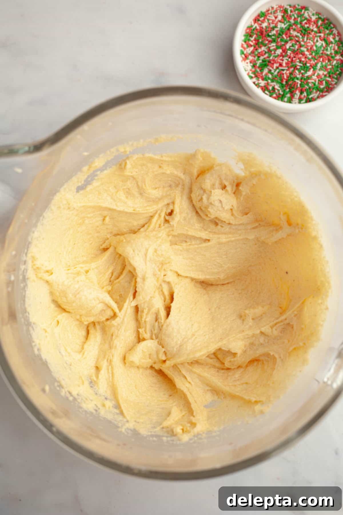 Melt-in-Your-Mouth Brown Butter Christmas Sprinkle Cookies 7 Cookie dough in a large glass bowl after eggs and vanilla have been added, showing a smooth, cohesive mixture.