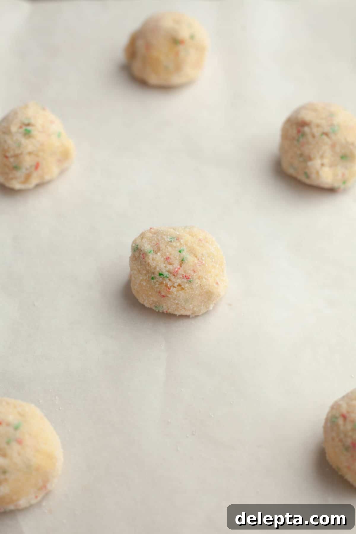 Melt-in-Your-Mouth Brown Butter Christmas Sprinkle Cookies 9 Sugar cookie dough balls rolled in granulated sugar and arranged on parchment paper on a baking sheet.