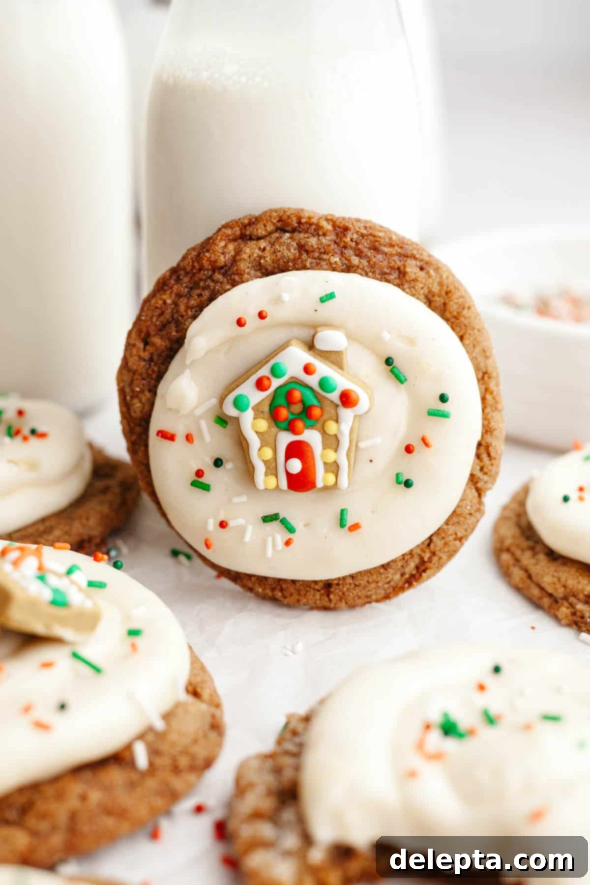 Velvet Gingerbread Cookies with Cream Cheese Frosting 12 A close-up of beautifully frosted gingerbread cookies, featuring smooth cream cheese frosting and a miniature gingerbread house decoration, ready for a holiday treat.