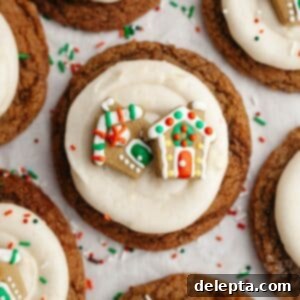 Velvet Gingerbread Cookies with Cream Cheese Frosting 14 A close up of a gingerbread cookie frosted with cream cheese frosting and a small gingerbread house decoration.