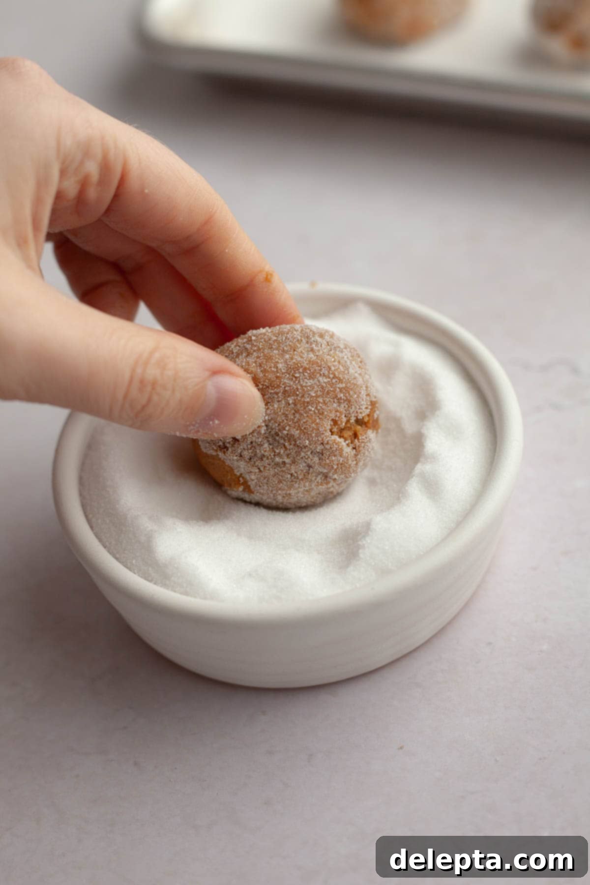 Velvet Gingerbread Cookies with Cream Cheese Frosting 8 A hand rolling a scoop of gingerbread cookie dough in a bowl of granulated sugar.