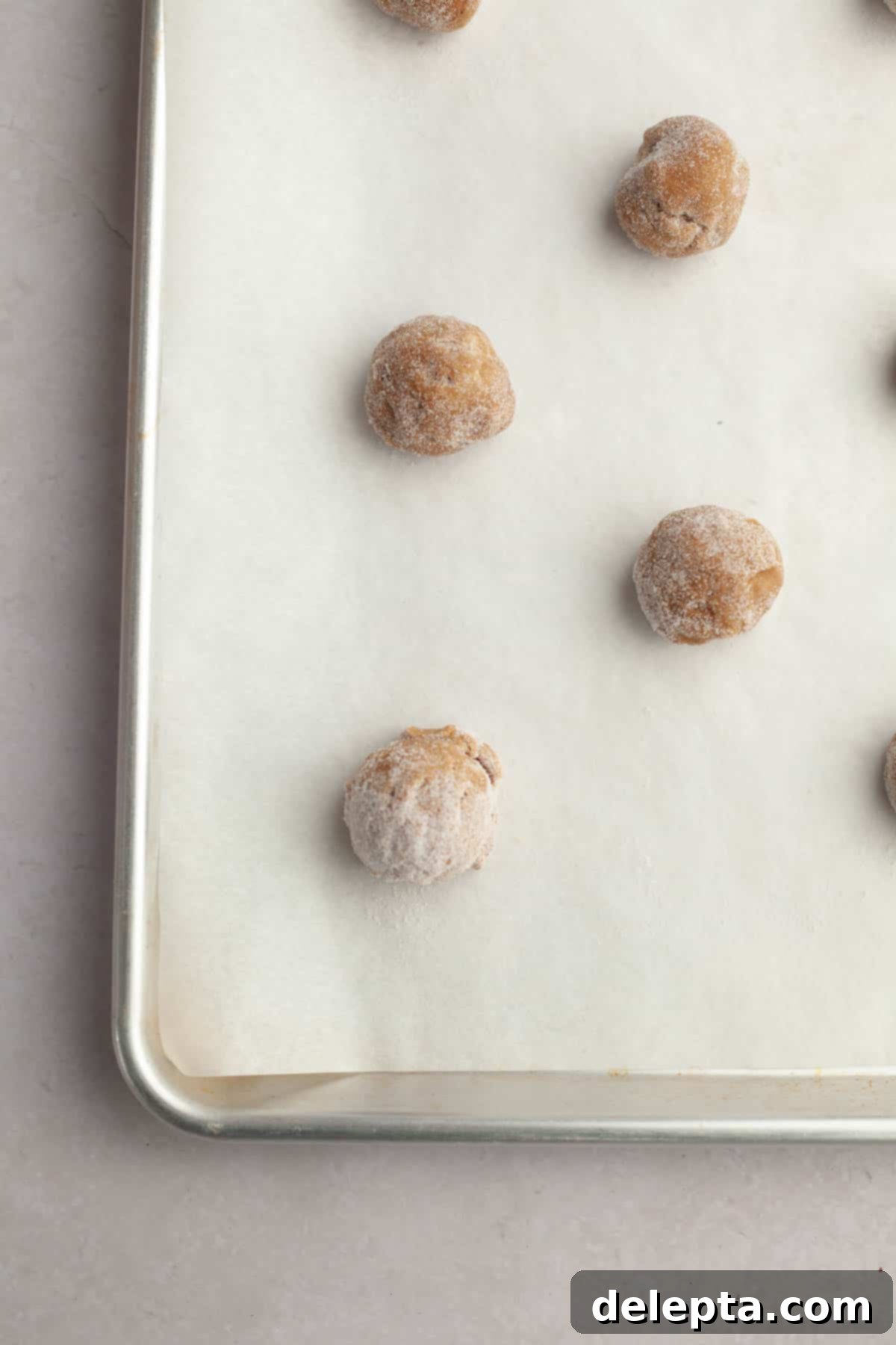 Velvet Gingerbread Cookies with Cream Cheese Frosting 9 Unbaked gingerbread cookie dough balls, coated in sugar, neatly spaced on parchment paper on a baking sheet.
