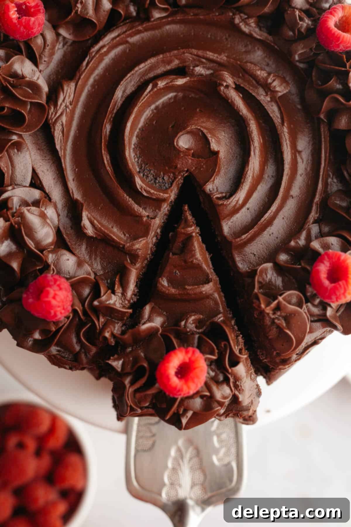 Moist and Easy Chocolate Cake with Decadent Chocolate Ganache 11 An overhead shot captures a slice of rich chocolate cake with a generous layer of chocolate ganache being carefully lifted out using a silver cake server, highlighting its moist layers and smooth frosting.
