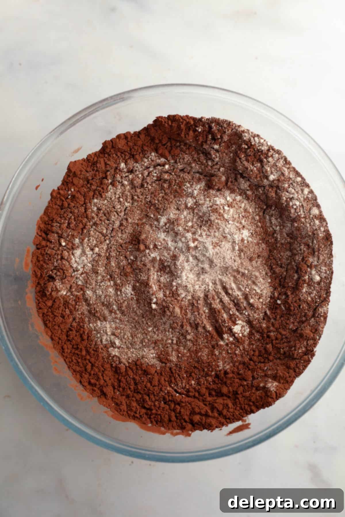 Moist and Easy Chocolate Cake with Decadent Chocolate Ganache 5 Dry ingredients including flour and rich Dutch-processed cocoa powder, carefully measured and resting in a large clear glass bowl, ready for mixing.