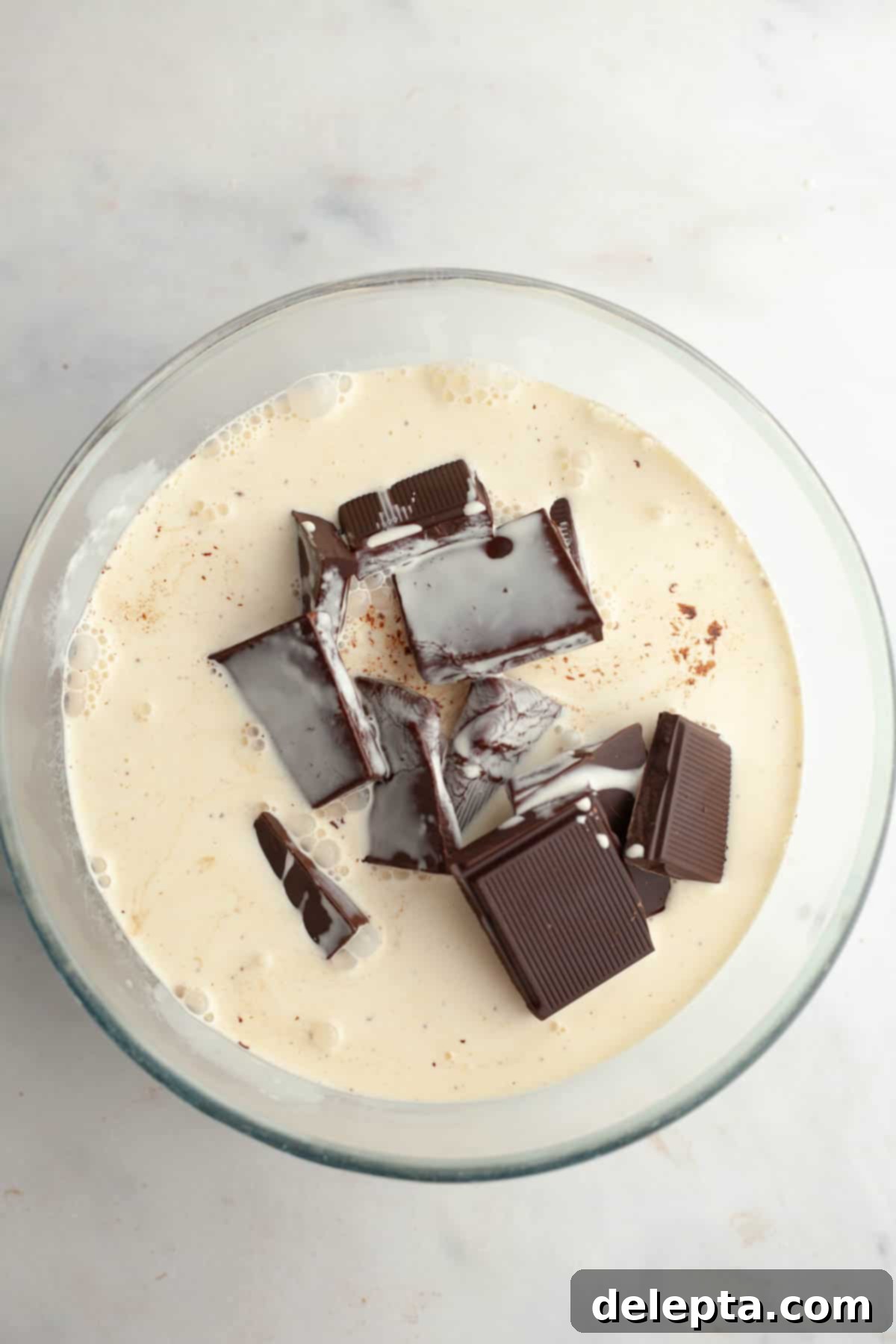 Moist and Easy Chocolate Cake with Decadent Chocolate Ganache 9 A close-up of chopped dark chocolate in a large bowl, with steaming hot heavy cream being poured directly over it, ready to melt the chocolate into a smooth ganache.