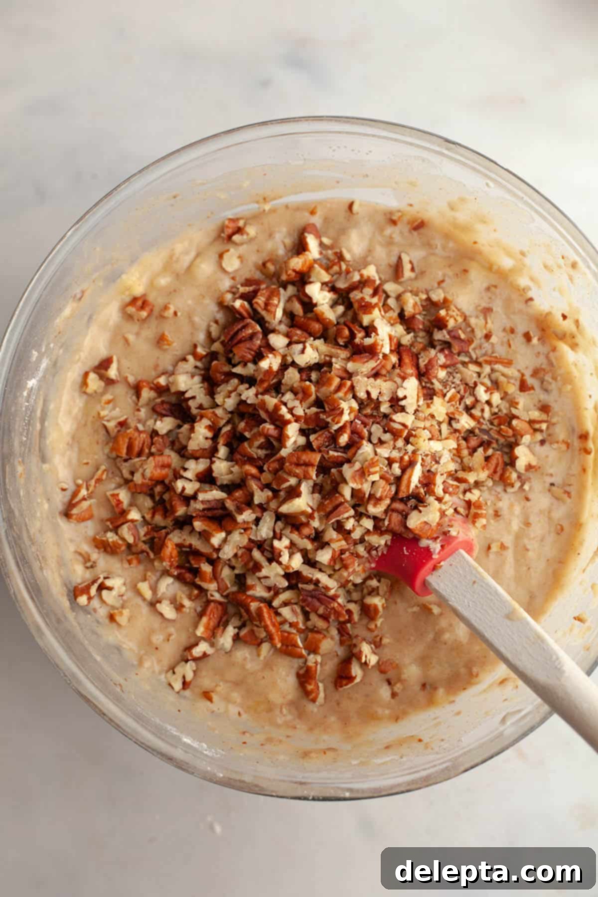 Decadent Brown Butter Cinnamon Pecan Banana Bread 7 Banana bread batter in a large glass mixing bowl with chopped pecans.