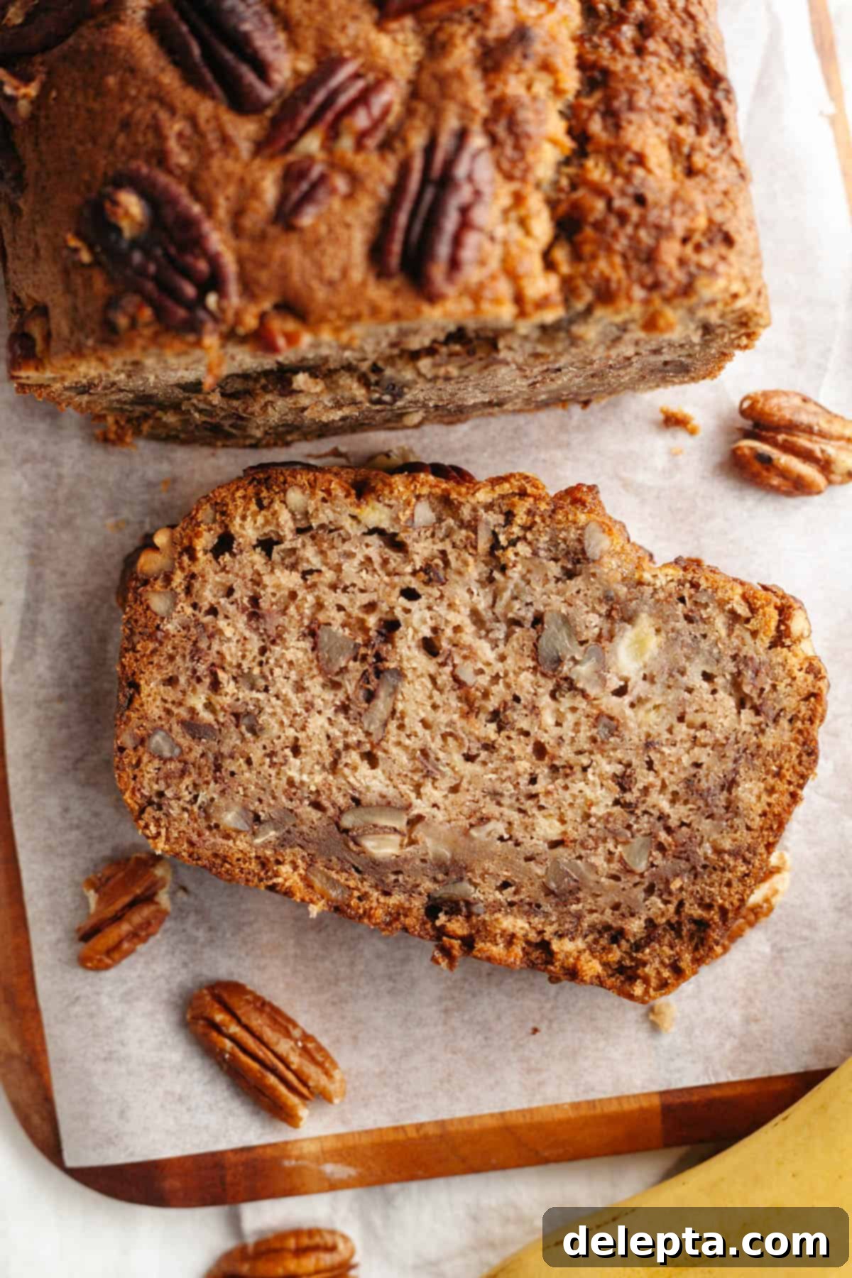 Decadent Brown Butter Cinnamon Pecan Banana Bread 10 A whole loaf of brown butter cinnamon pecan banana bread on a wooden cutting board, with a few slices cut.