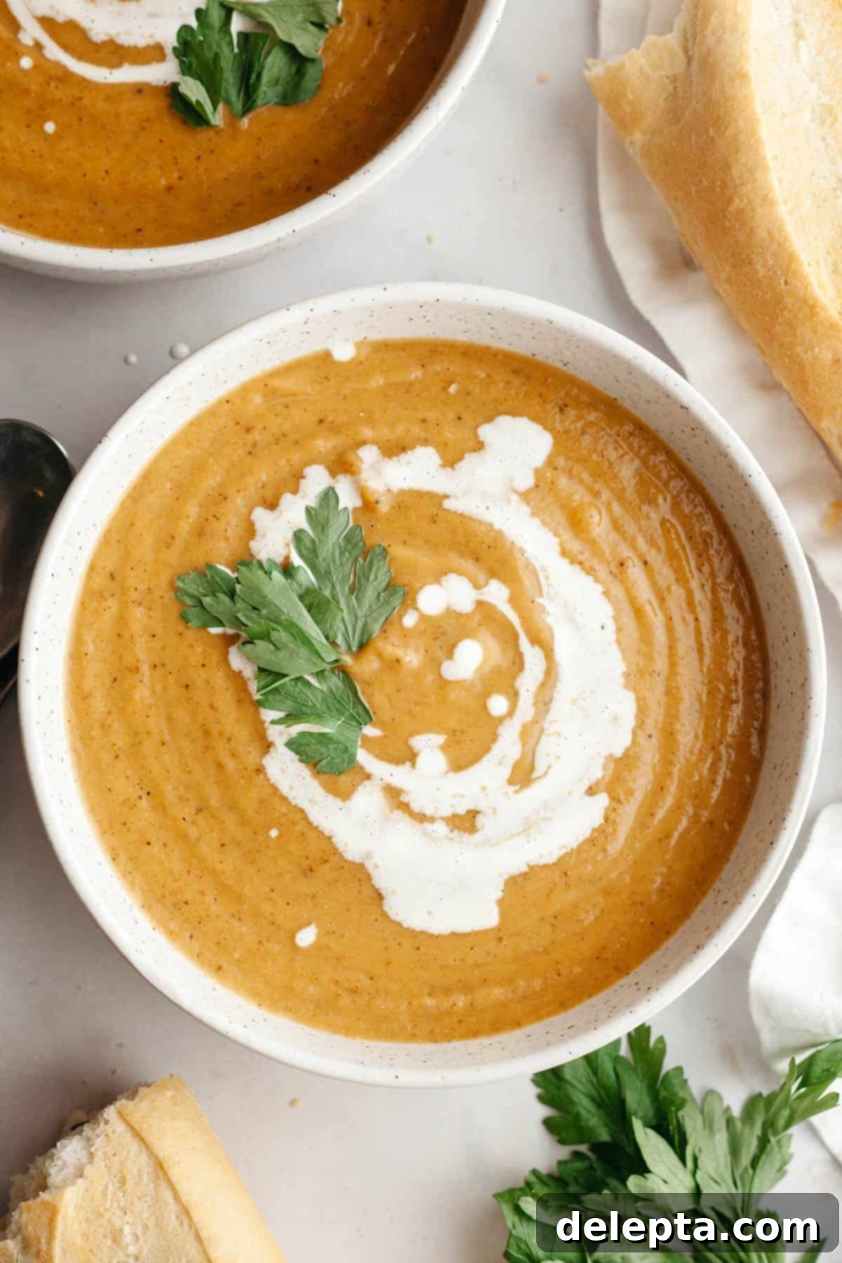 Velvety Roasted Butternut Cauliflower Soup 2 A white soup bowl with roasted butternut squash cauliflower soup, drizzled with cream and garnished with fresh herbs.
