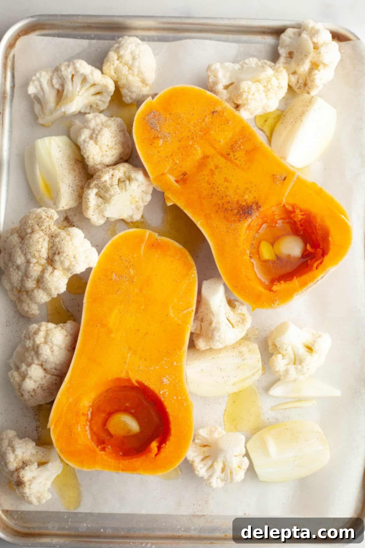 Velvety Roasted Butternut Cauliflower Soup 4 A sheet pan with a butternut squash cut in half, chopped yellow onions and cauliflower florets, drizzled with olive oil and seasoned with pepper.