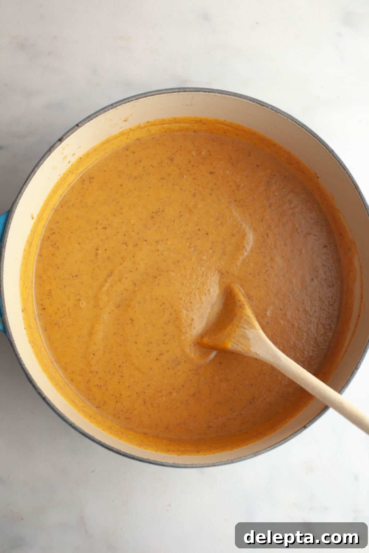 Velvety Roasted Butternut Cauliflower Soup 7 A large dutch oven filled with creamy butternut squash cauliflower soup, with a wooden spoon resting in it.