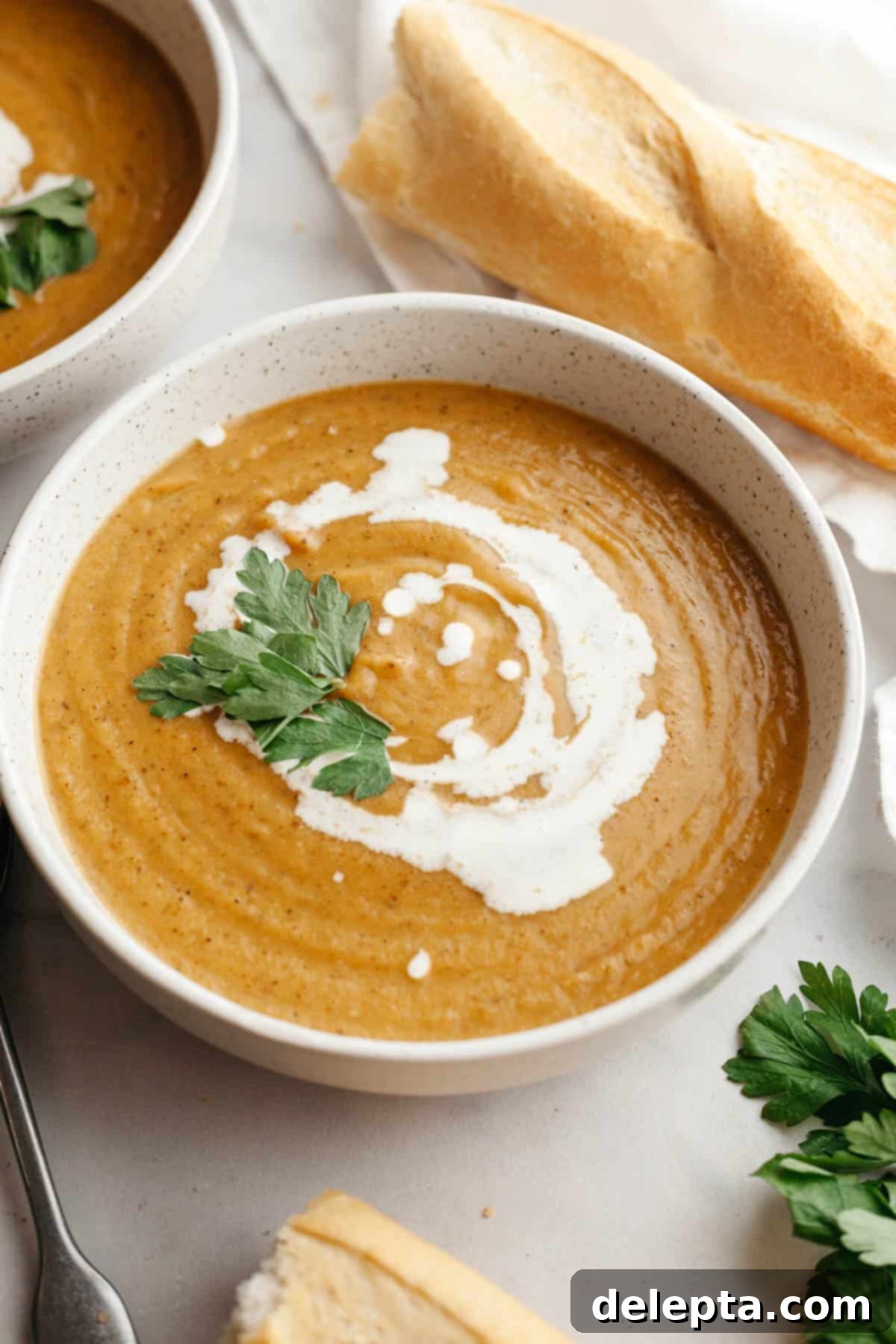 Velvety Roasted Butternut Cauliflower Soup 9 A white soup bowl with creamy butternut squash cauliflower soup, drizzled with cream and garnished with fresh herbs, ready to be served.