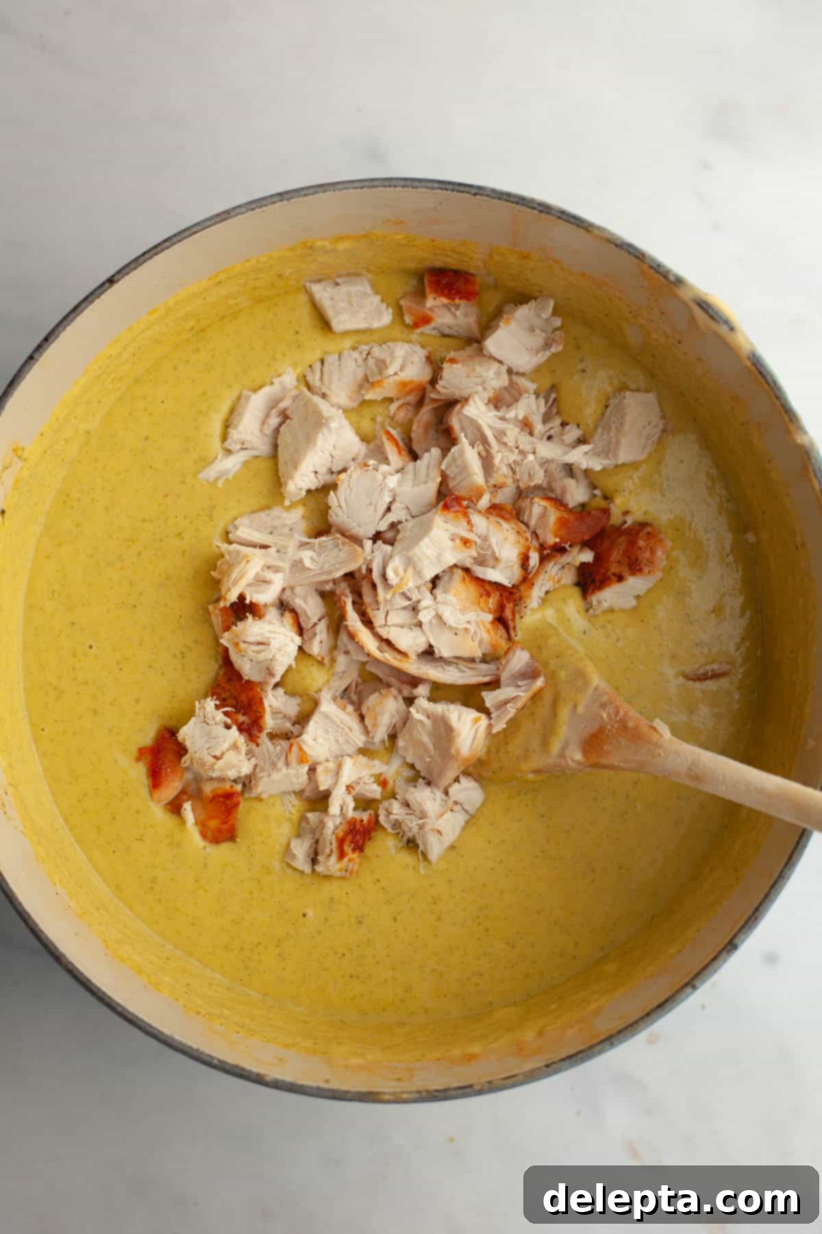 Velvety Chicken and Broccoli Cheddar Soup 11 A large dutch oven filled with creamy broccoli cheddar soup, with cooked chicken pieces mixed in, ready to be served.