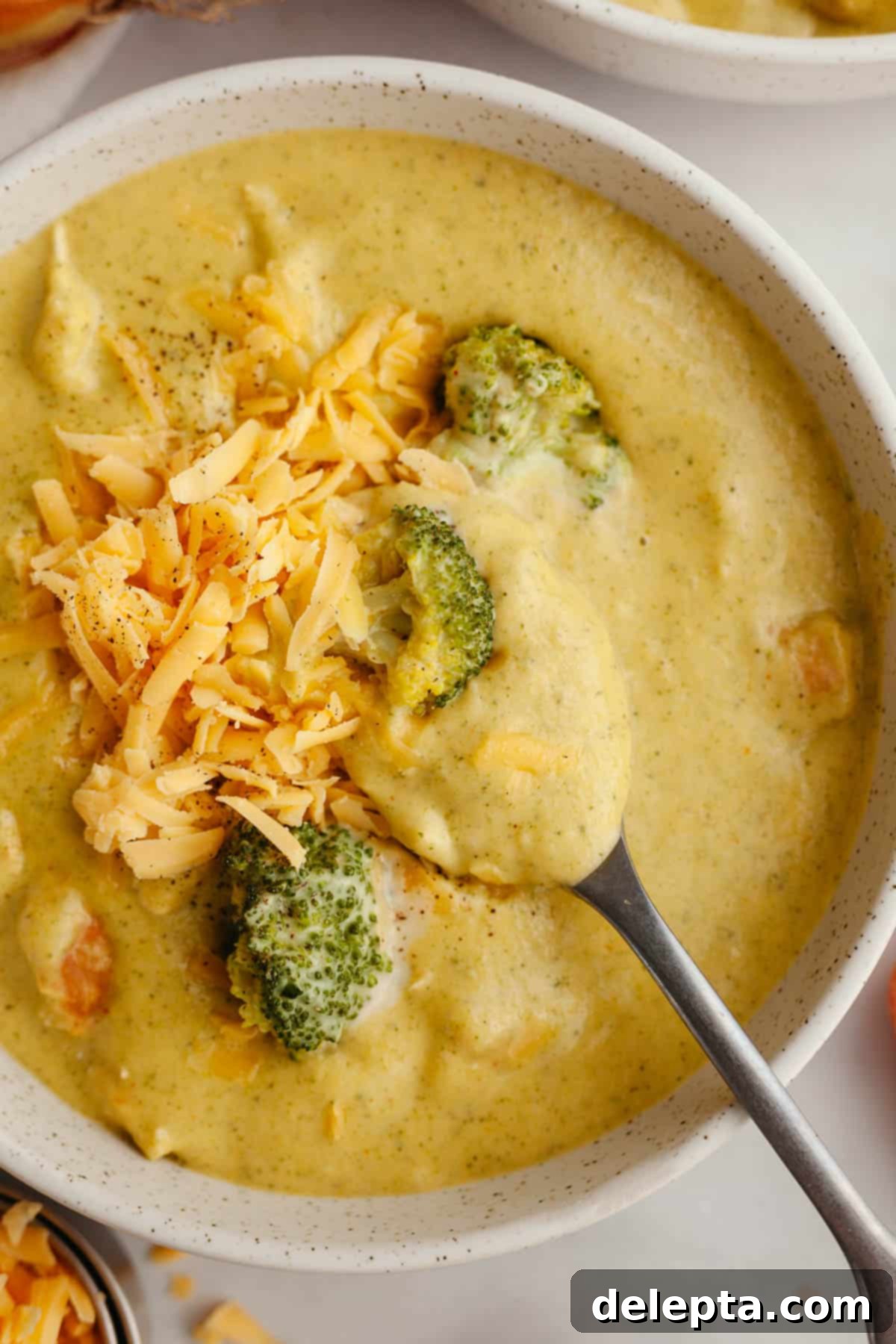 Velvety Chicken and Broccoli Cheddar Soup 12 A beautifully presented bowl of chicken and broccoli cheddar soup, garnished with extra shredded cheddar cheese and a sprig of fresh dill.