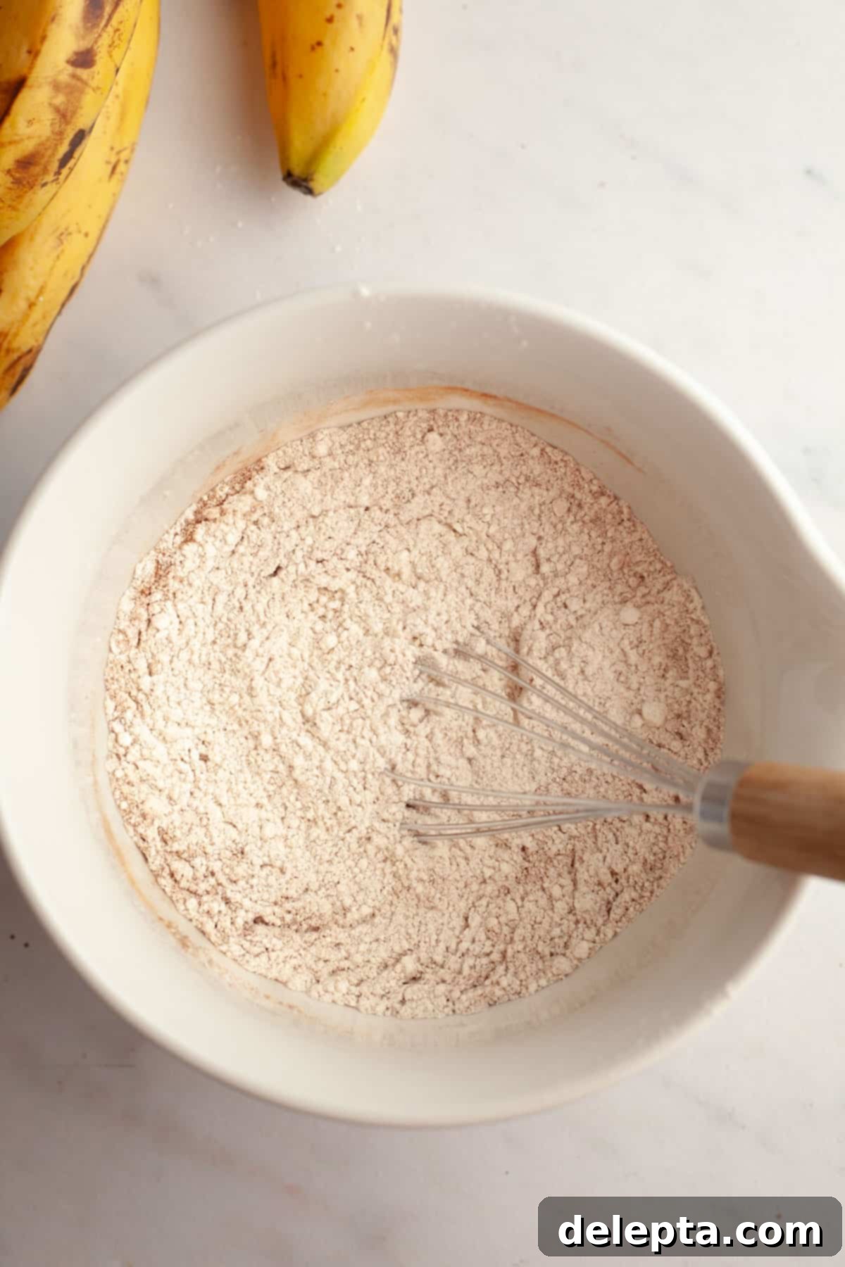 Bakery Style Jumbo Banana Chocolate Chip Muffins 5 A bowl with flour in it with a whisk, showing the dry ingredients.
