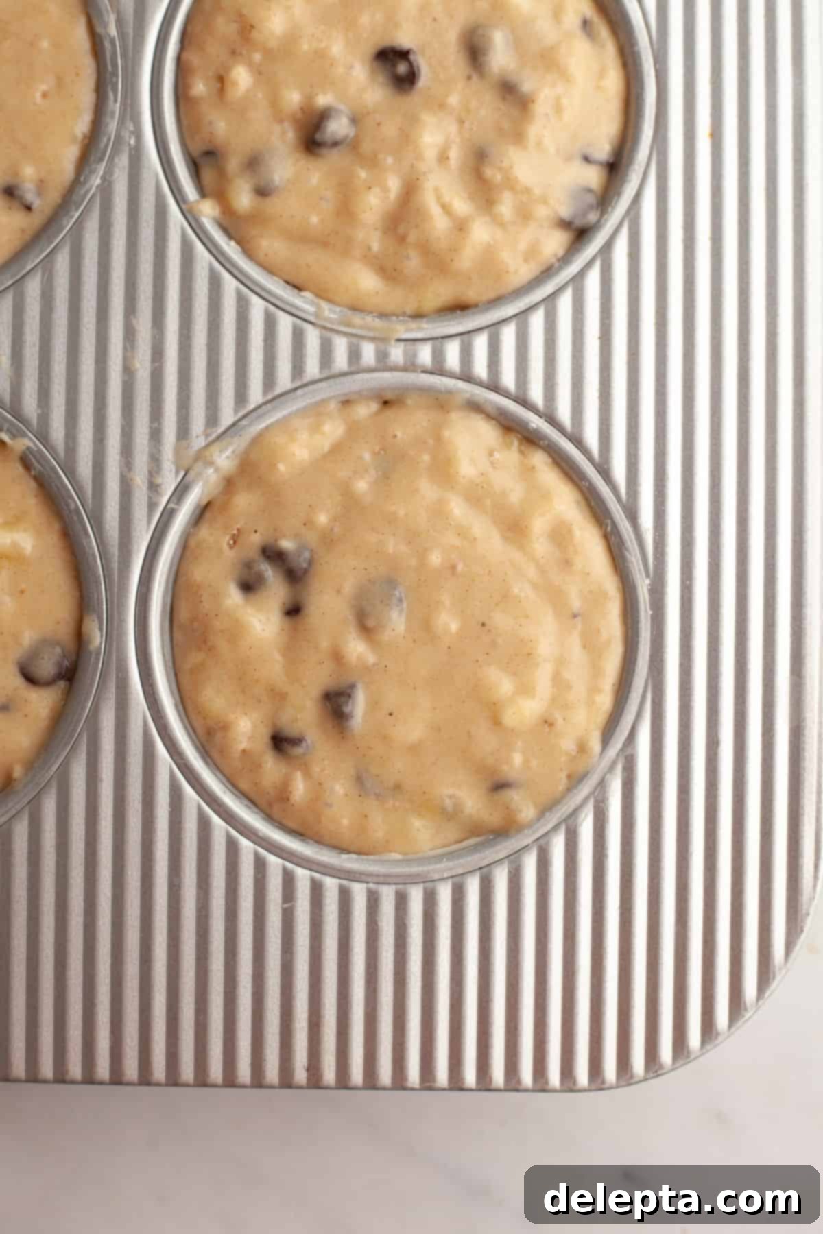 Bakery Style Jumbo Banana Chocolate Chip Muffins 8 Unbaked chocolate chip banana muffins in a jumbo muffin pan, filled to the brim.