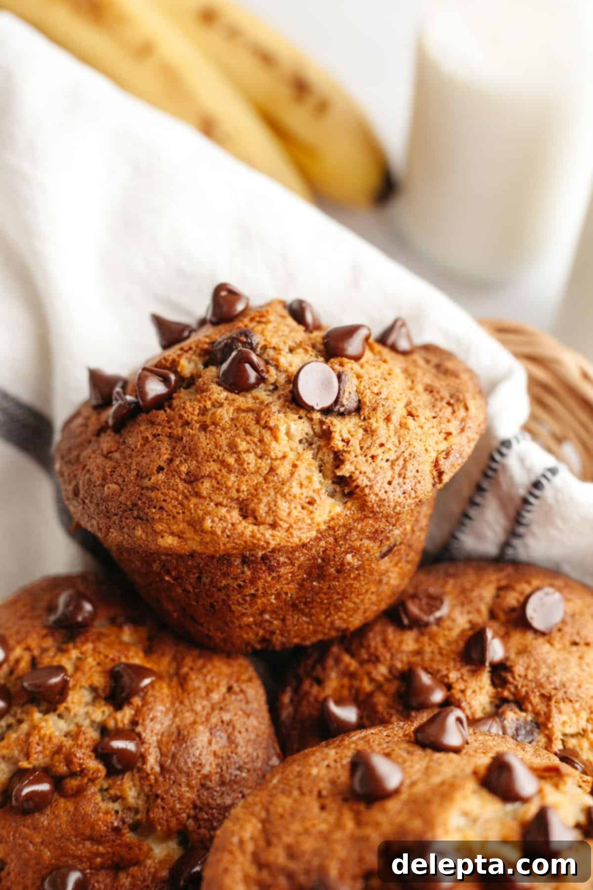 Bakery Style Jumbo Banana Chocolate Chip Muffins 9 A close up of freshly baked chocolate chip banana jumbo muffins in a basket, golden brown with tall tops.
