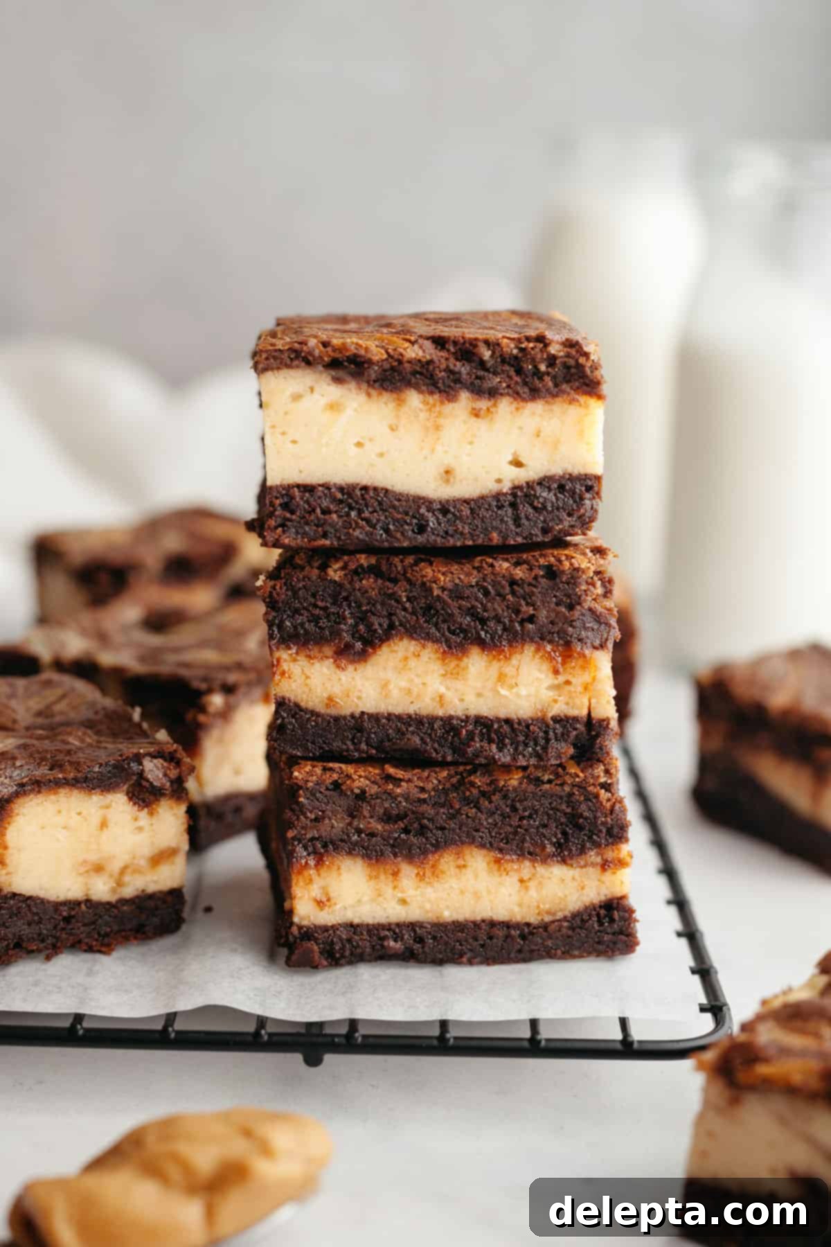 Decadent Peanut Butter Cream Cheese Swirl Brownies 2 A stack of three peanut butter cheesecake brownies on parchment paper, showcasing the beautiful swirl.