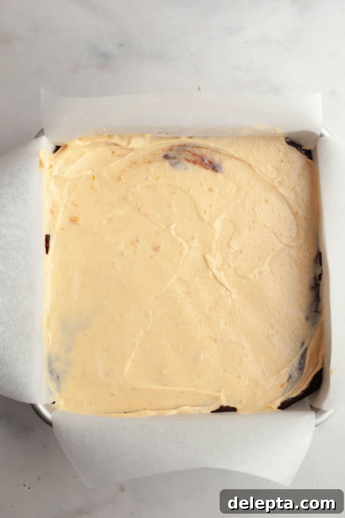 Decadent Peanut Butter Cream Cheese Swirl Brownies 9 A square pan lined with parchment paper with brownies and peanut butter cheesecake batter on top, ready to be swirled.