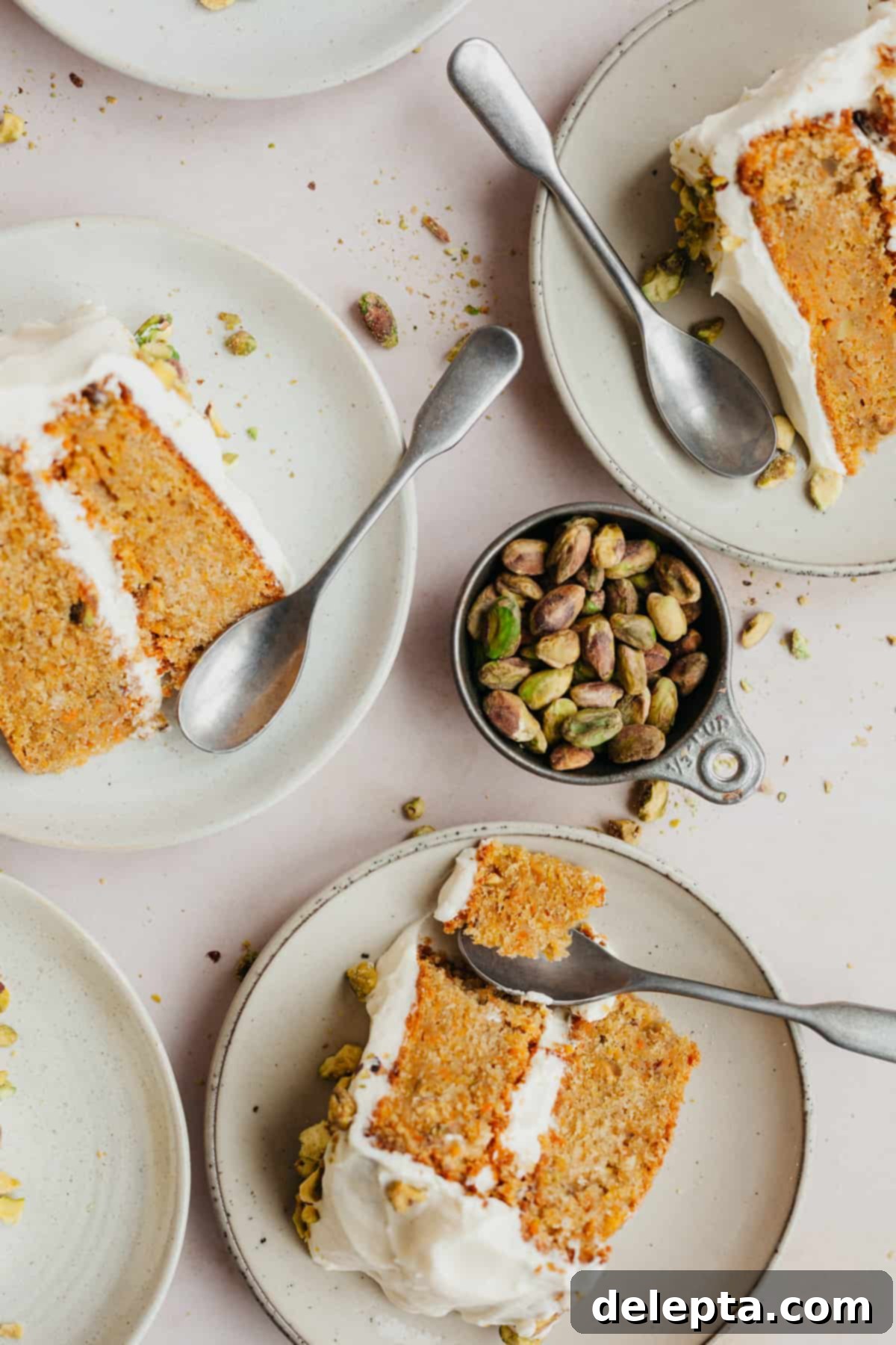 Pistachio-Infused Carrot Cake with Cloud-Like Cream Cheese Frosting 11 Three small plates with slices of carrot cake on each plate and a small spoon. There is a metal measuring cup filled with pistachios.