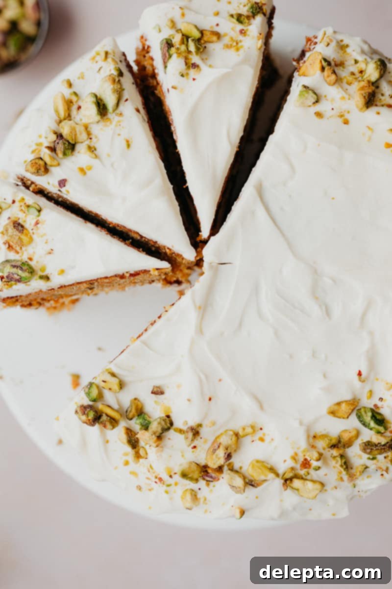 Pistachio-Infused Carrot Cake with Cloud-Like Cream Cheese Frosting 12 An overhead shot of a frosted carrot cake decorated with pistachios, Three slices have been made.