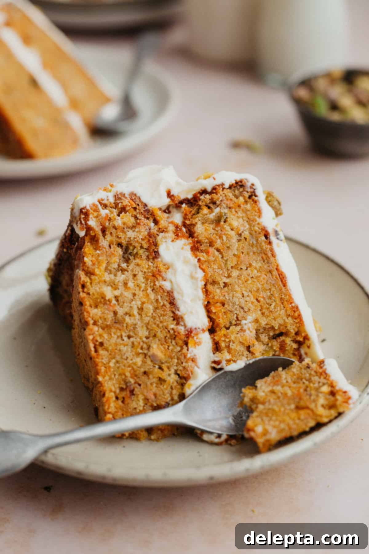 Pistachio-Infused Carrot Cake with Cloud-Like Cream Cheese Frosting 13 A slice of layered carrot cake with a small spoon scooping out a piece