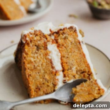 Pistachio-Infused Carrot Cake with Cloud-Like Cream Cheese Frosting 14 A slice of layered carrot cake with a small spoon scooping out a piece