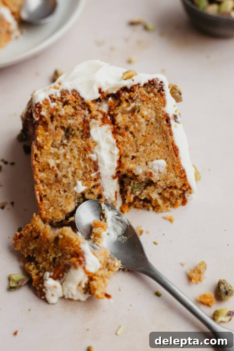 Pistachio-Infused Carrot Cake with Cloud-Like Cream Cheese Frosting 3 A slice of layered carrot cake with a small spoon scooping out a piece