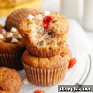 Effortless Banana Raspberry White Chocolate Chip Muffins 11 Two raspberry banana muffins stacked on top of each other, one has a bite taken out of it.