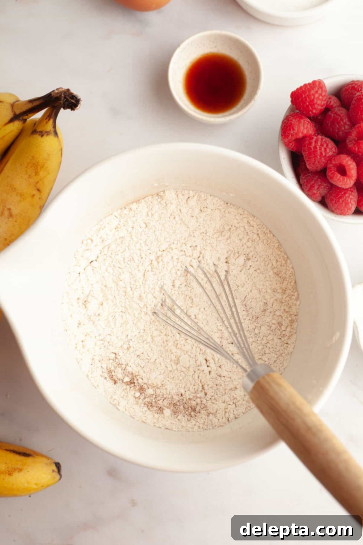 Effortless Banana Raspberry White Chocolate Chip Muffins 4 A white bowl with a whisk and flour in it, ready for mixing dry ingredients.