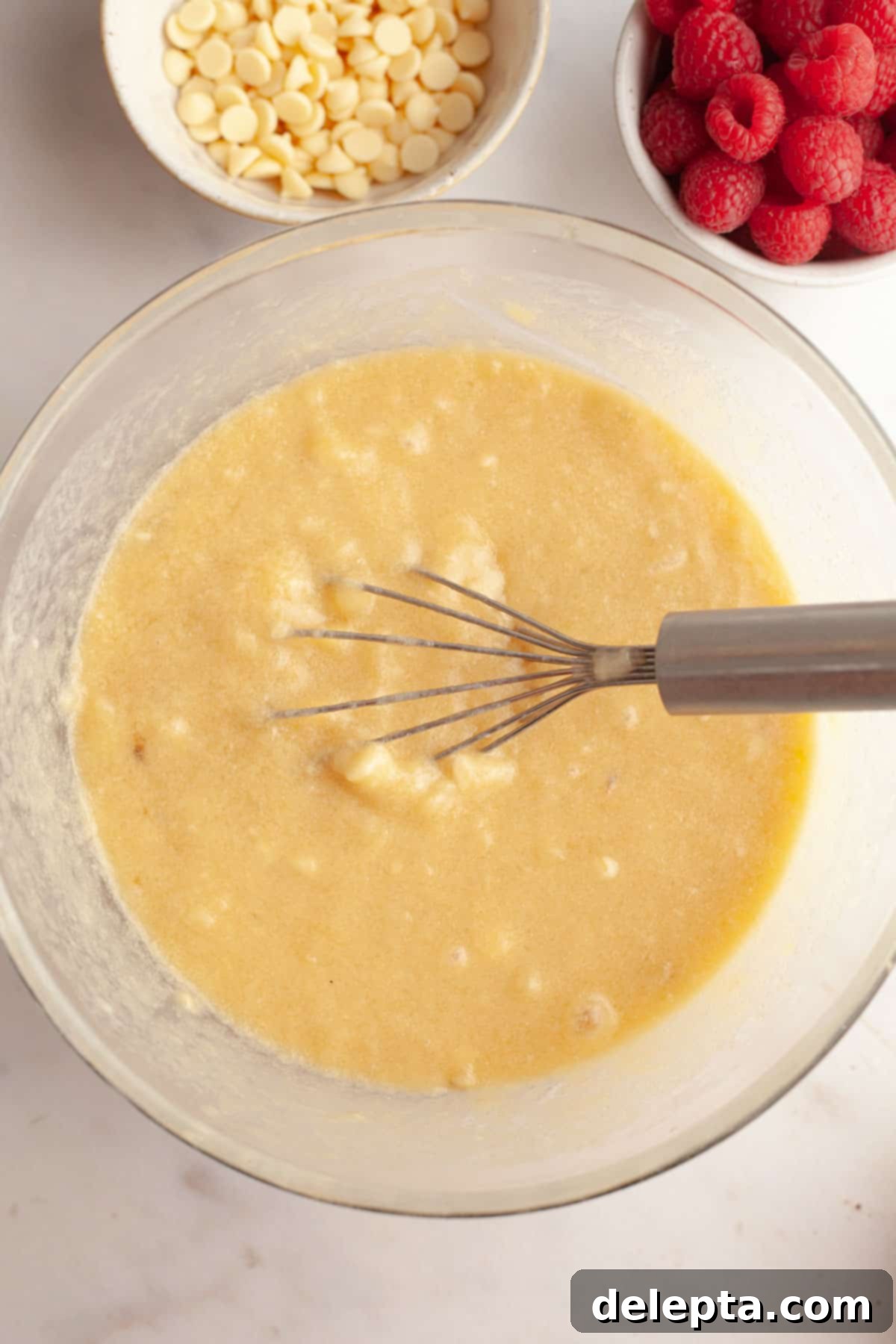 Effortless Banana Raspberry White Chocolate Chip Muffins 6 A bowl with banana muffin batter in it and a whisk, showing the mixture of wet ingredients.