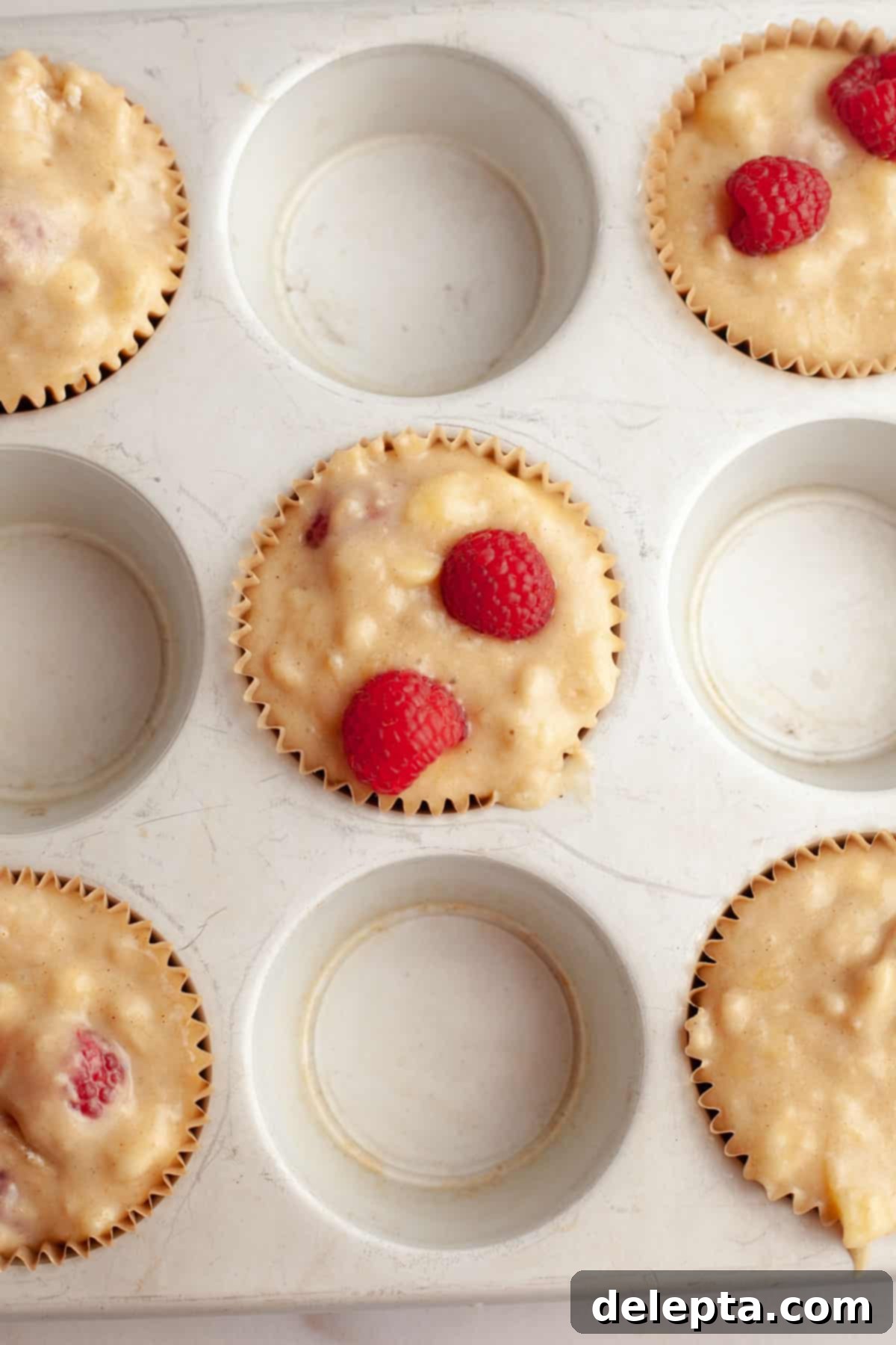 Effortless Banana Raspberry White Chocolate Chip Muffins 8 Unbaked banana raspberry muffins, generously filled in a muffin pan, with some extra raspberries on top.