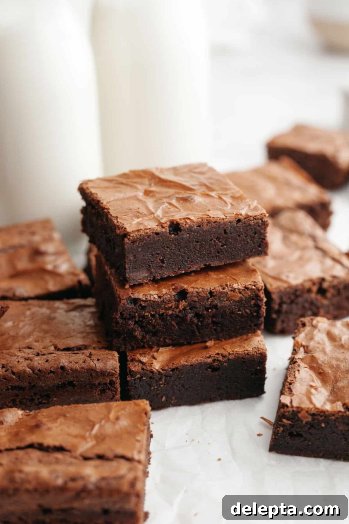 Easy Double Fudge Brownies Better Than Any Bakery 2 A stack of three double fudge brownies on parchment paper, showcasing their perfect crinkle tops and rich color.
