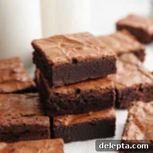 Easy Double Fudge Brownies Better Than Any Bakery 13 A stack of three double fudge brownies on parchment paper, perfectly baked with a shiny crinkle top.