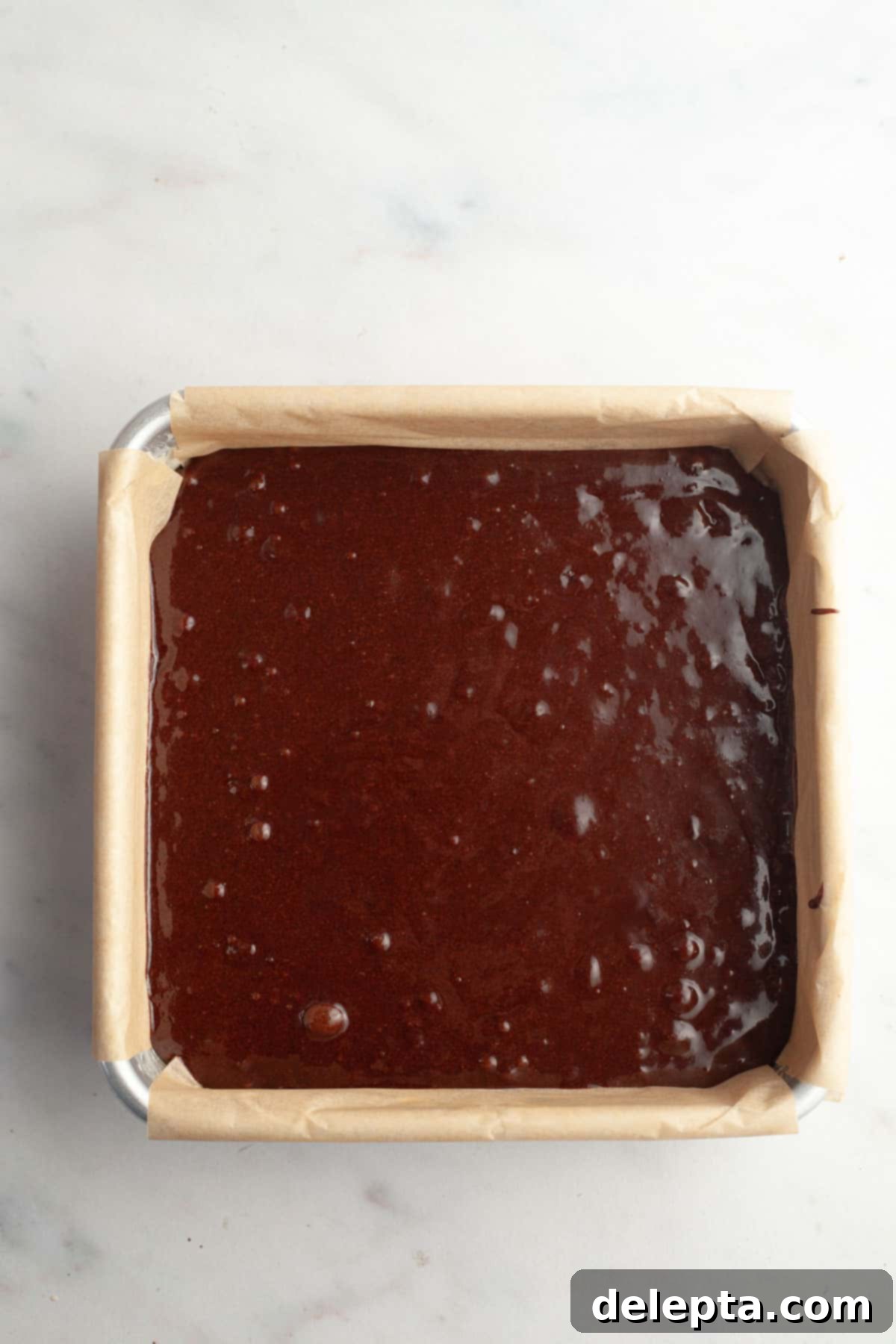 Easy Double Fudge Brownies Better Than Any Bakery 10 Unbaked brownie batter poured evenly into a square baking pan lined with parchment paper.