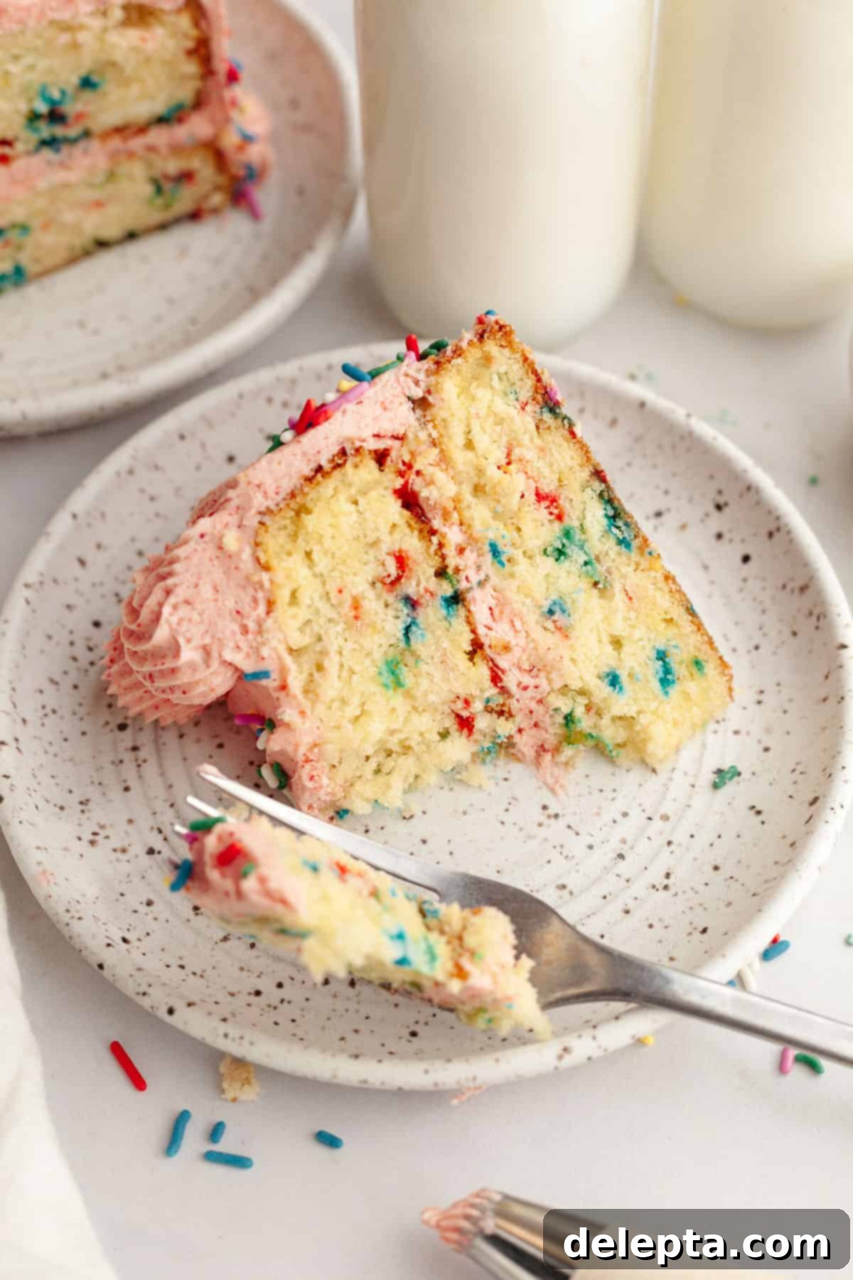 Strawberry Funfetti Fantasy 13 A delectable slice of strawberry funfetti cake on a small plate, with a bite taken out, showing the moist interior.