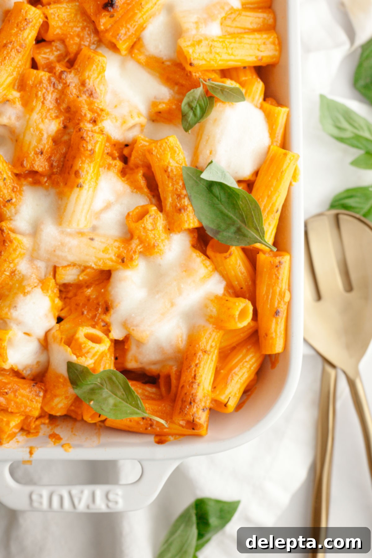 Easy Baked Pasta with Virgin Vodka Sauce 11 A white baking dish filled with cheesy baked vodka pasta, garnished with fresh basil leaves, ready to be enjoyed.