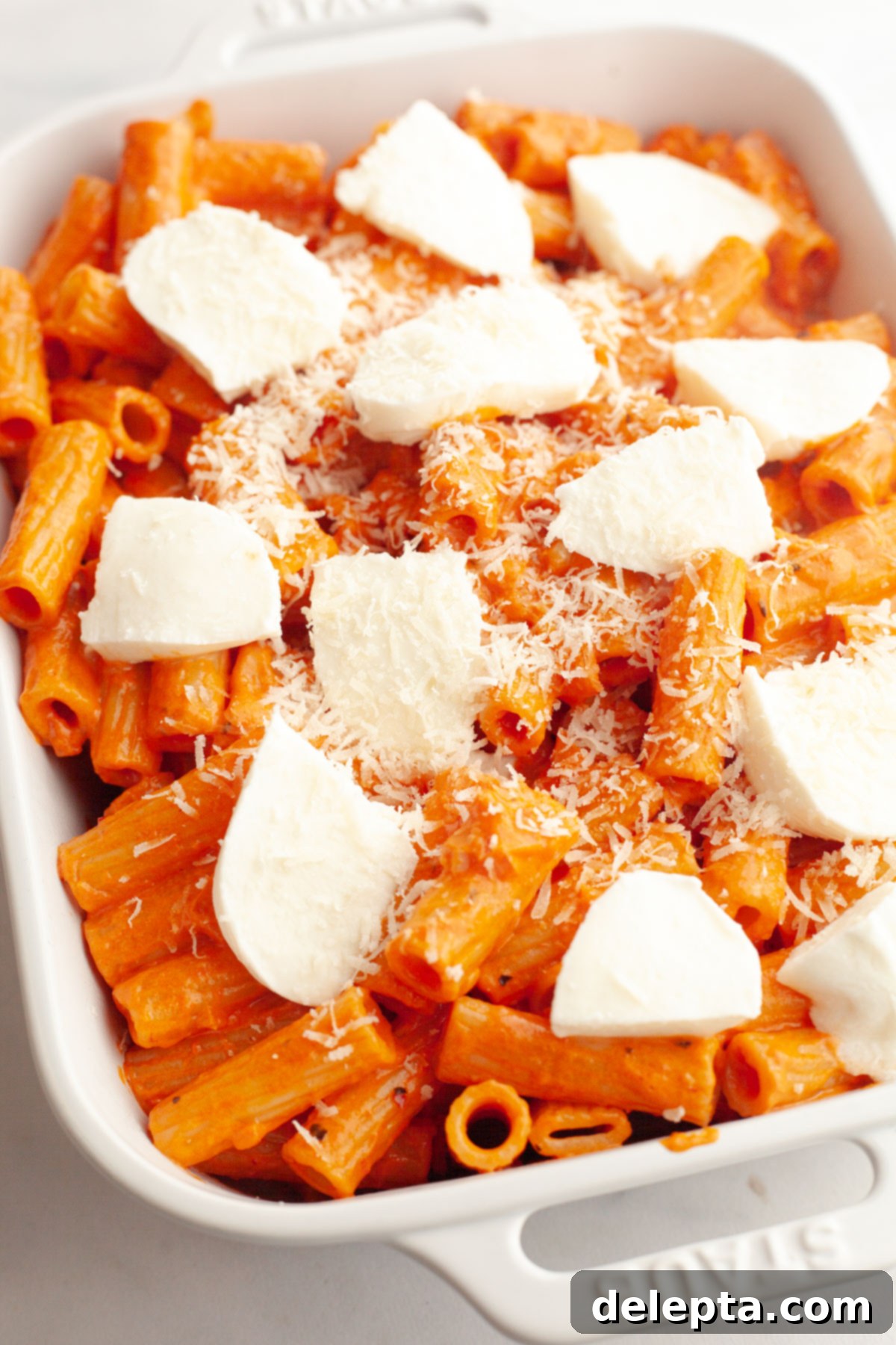 Easy Baked Pasta with Virgin Vodka Sauce 9 Vodka pasta in a white baking dish topped with fresh mozzarella slices and extra grated parmesan, ready for baking.