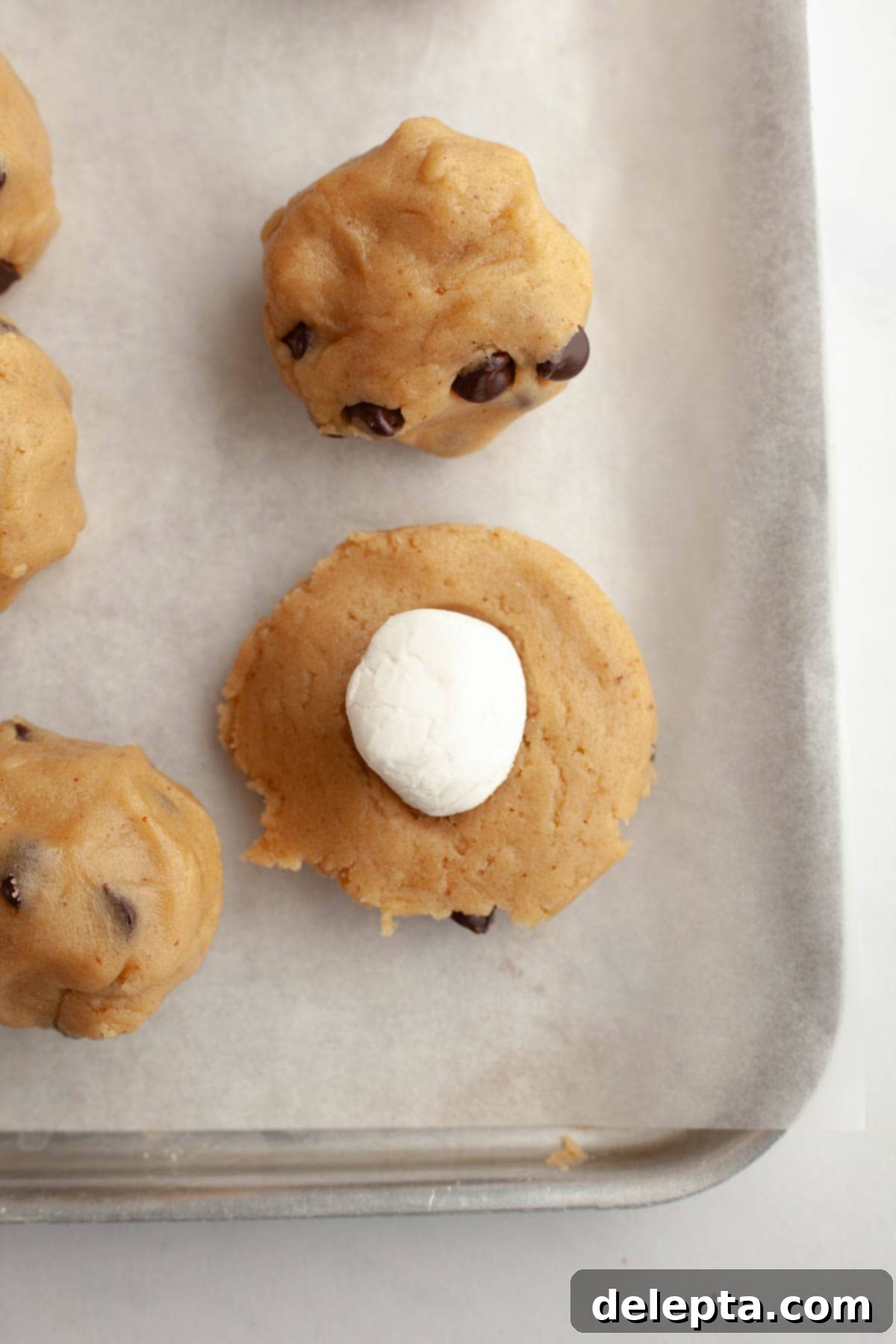 Gooey Chocolate Chip Marshmallow Cookies 7 A round piece of cookie dough, flattened into a disc, with a perfectly frozen marshmallow placed on its center, ready to be wrapped.