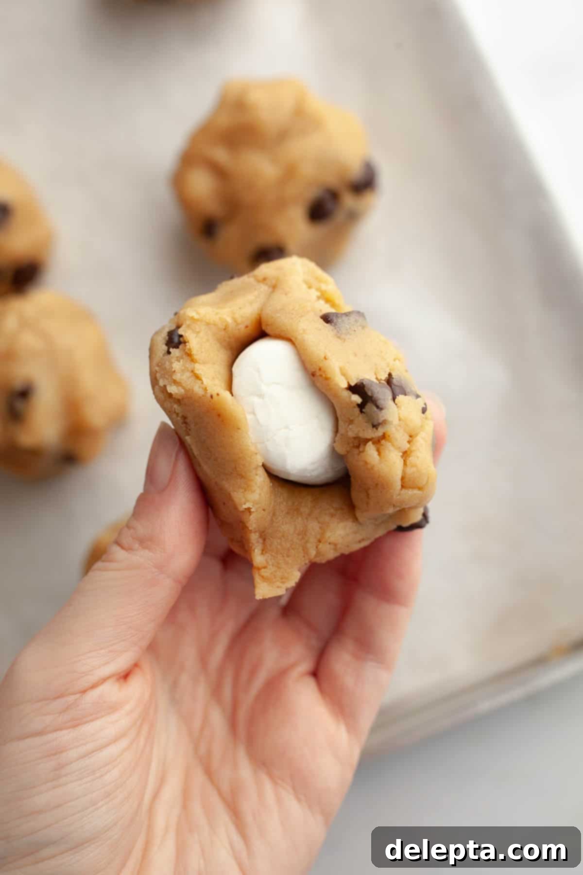 Gooey Chocolate Chip Marshmallow Cookies 8 A hand carefully folding and molding cookie dough around a frozen marshmallow, creating a perfectly sealed, smooth dough ball.